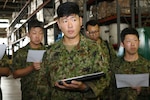 Japanese Ground Self Defense Force officers in a warehouse listen to a briefing.
