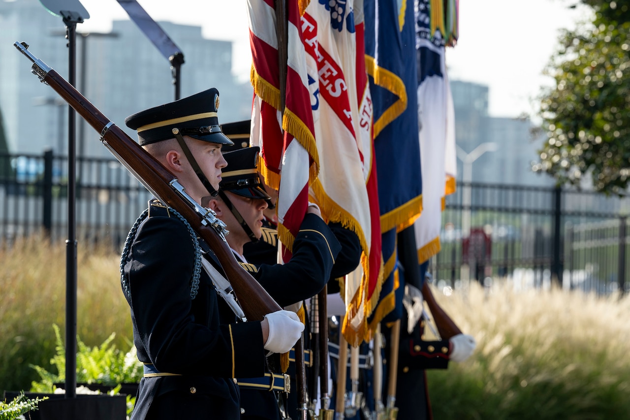 Members of a color guard stand in a row holding flags and ceremonial weapons.