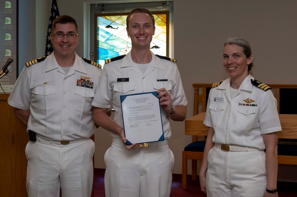 240910-N-DF135-1002 Lt. Timothy Fellin (center) is presented with his graduation certificate by Capt. Brian Feldman, NMCP director/Navy Medicine Readiness and Training Command Portsmouth commander, and Cmdr. Robyn Treadwell, NMCP’s Mental Health director.  Fellin will be stationed at Naval Nuclear Power Training Command, South Carolina.