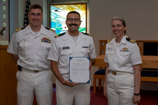 240910-N-DF135-1005 Lt. Nathaniel Sanchez (center) is presented with his graduation certificate by Capt. Brian Feldman, NMCP director/Navy Medicine Readiness and Training Command Portsmouth commander, and Cmdr. Robyn Treadwell, NMCP’s Mental Health director. Sanchez will be stationed at Embedded Mental Health Postdoctoral Fellowship, San Diego.