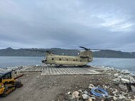 An Alaska Army National Guard CH-47 Chinook lands for the first time on Little Diomede, Alaska, with Big Diomede, Russia, visible in the background. The unit supported Operation Polar Dagger, a joint special operations mission across the Alaskan Arctic.