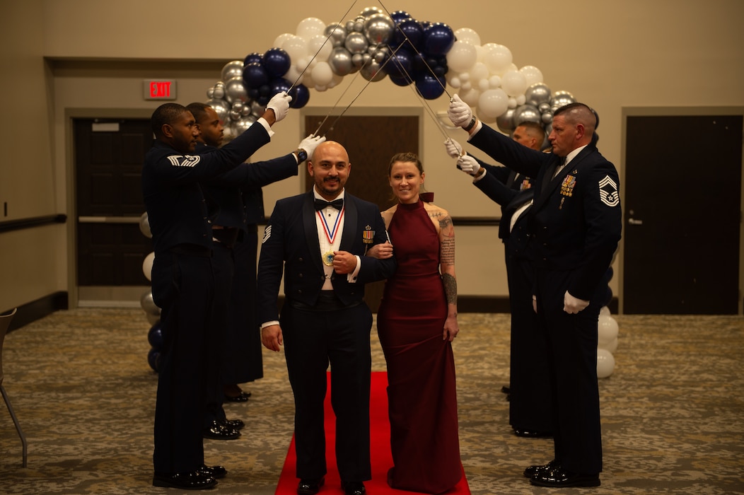 U.S. Air Force Master Sgt. Cedric J. Abolos, 75th Fighter Generation Squadron maintenance noncommissioned officer in charge, walks through a saber arch with his wife during a senior noncommissioned officer induction ceremony at the Valdosta State University Ballroom, Valdosta, Georgia, Sept. 05, 2024. A Saber Arch is a formation where several individuals hold their sabers raised, creating an archway that the newly promoted SNCOs walk through, signifying their official entrance into the senior enlisted ranks. (U.S. Air Force photo by Airman 1st Class Iain Stanley)