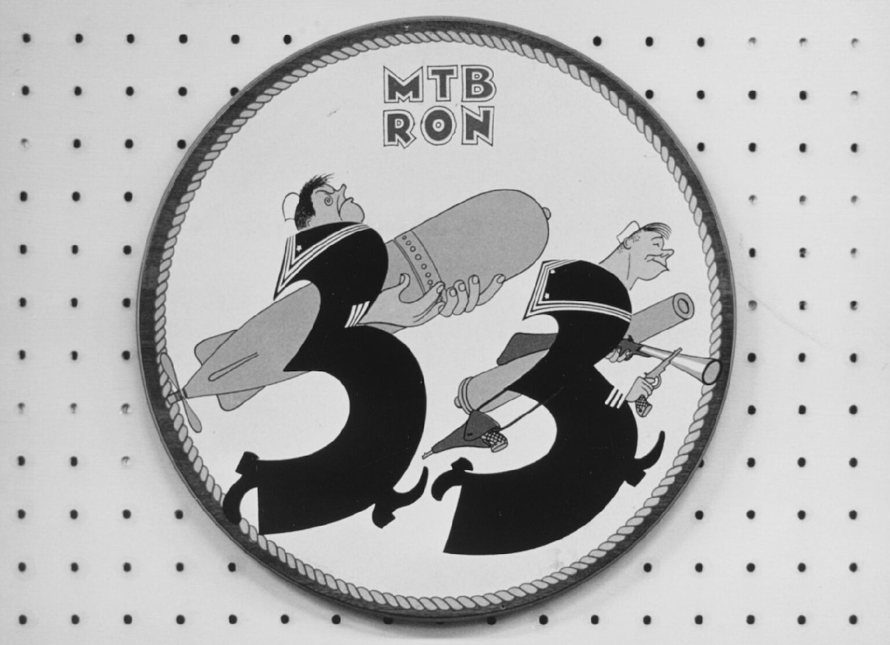 An insignia shows two cartoon men carry large torpedoes.