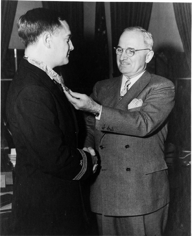 A man holds the medal around another man’s neck.