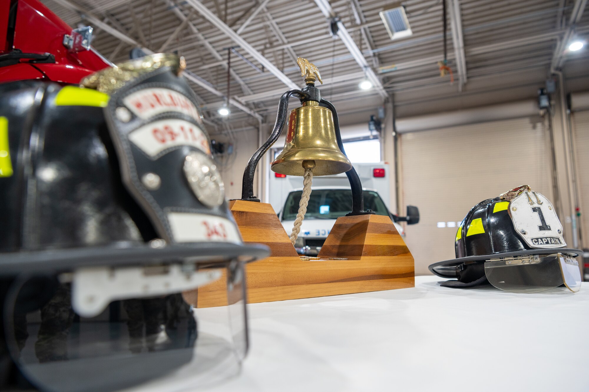 Two firefighter helmets and a large bell are displayed on a table during a 9/11 remembrance ceremony at Hurlburt Field, Florida, Sept. 11, 2024.