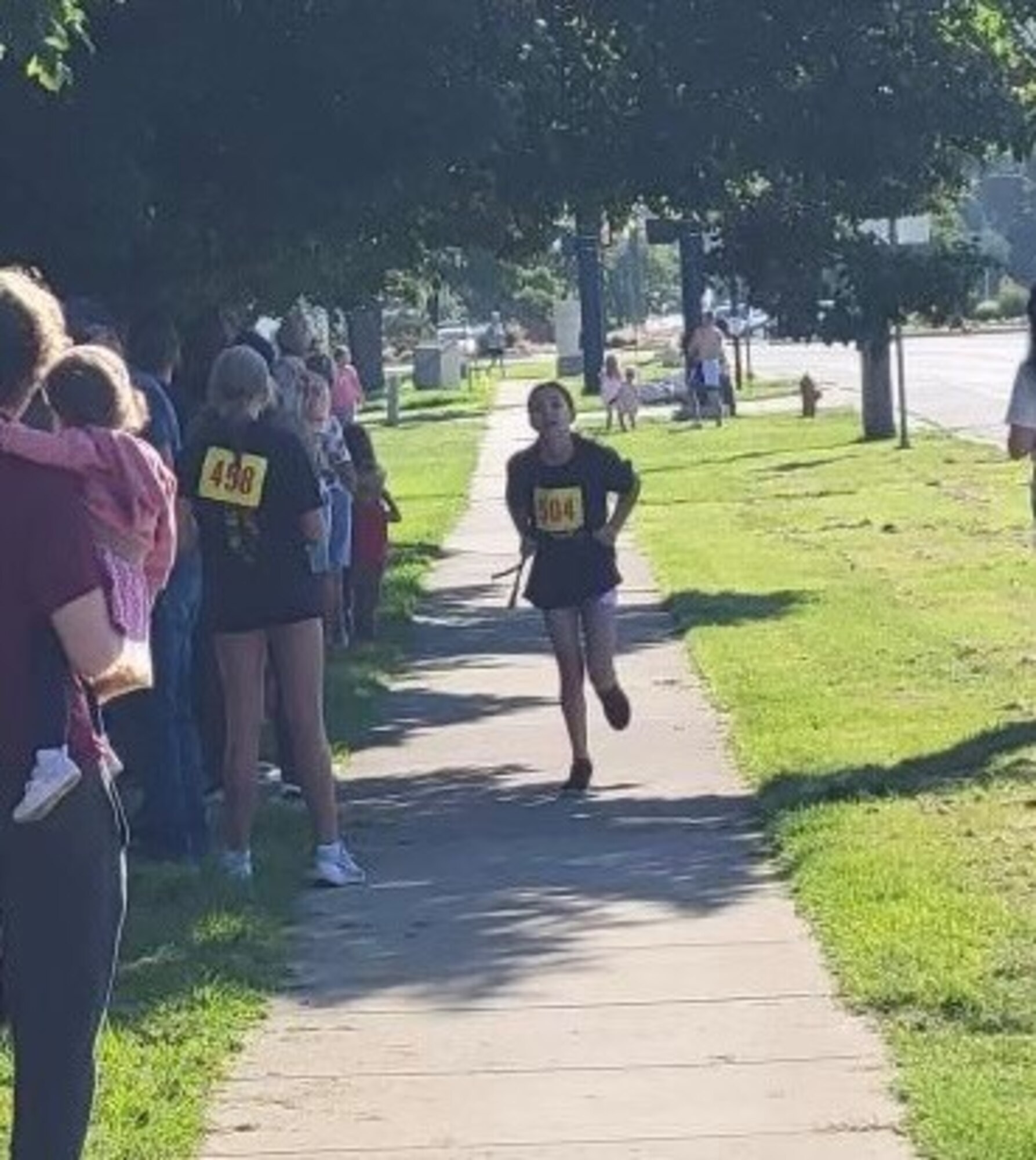 A gilr runs along a sidewalk with spectators cheering
