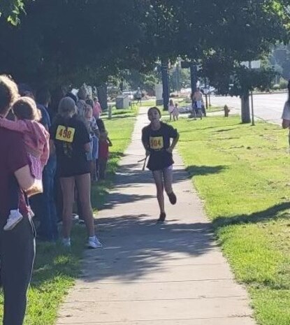A gilr runs along a sidewalk with spectators cheering