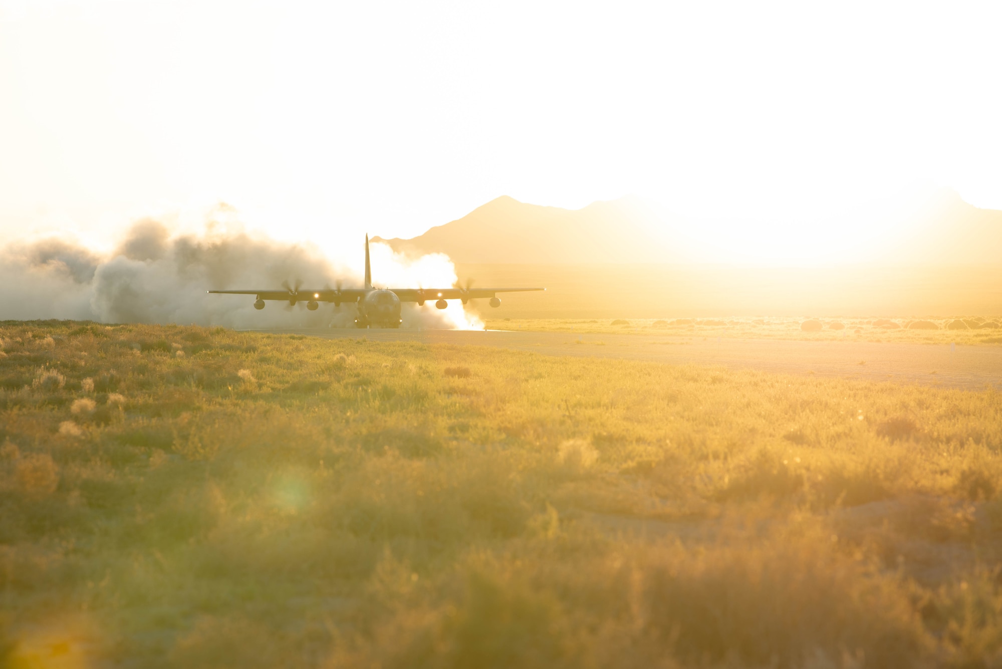 A military cargo aircraft lands on a dusty dirt landing strip.
