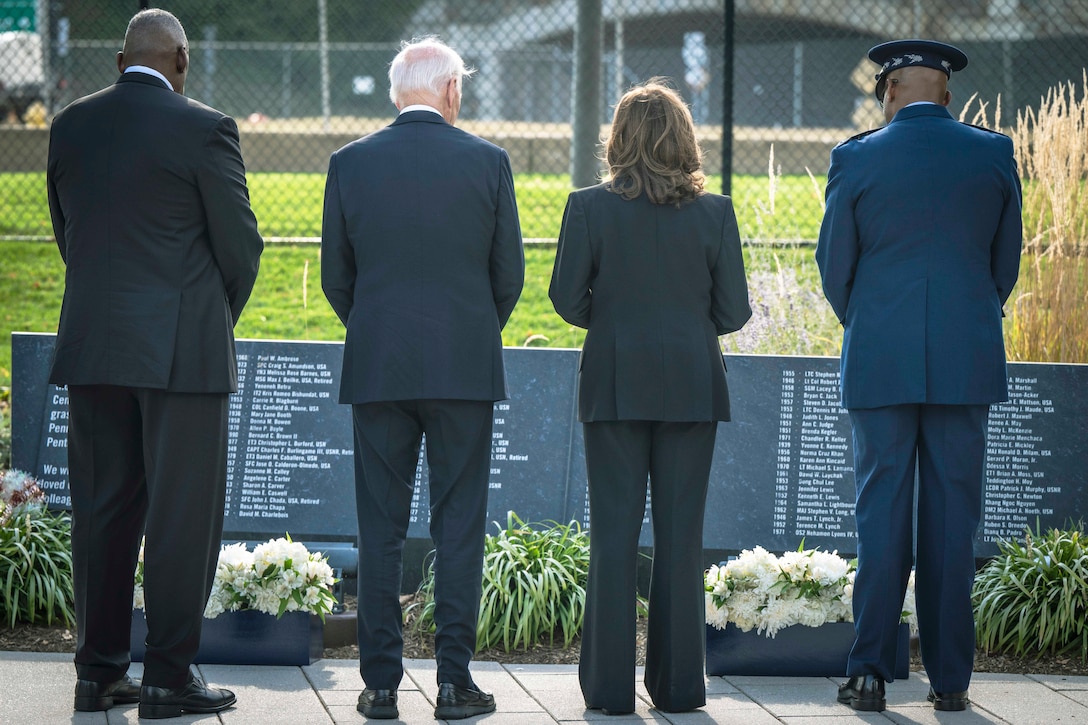 Four U.S. leaders stand in formation in front of a memorial.