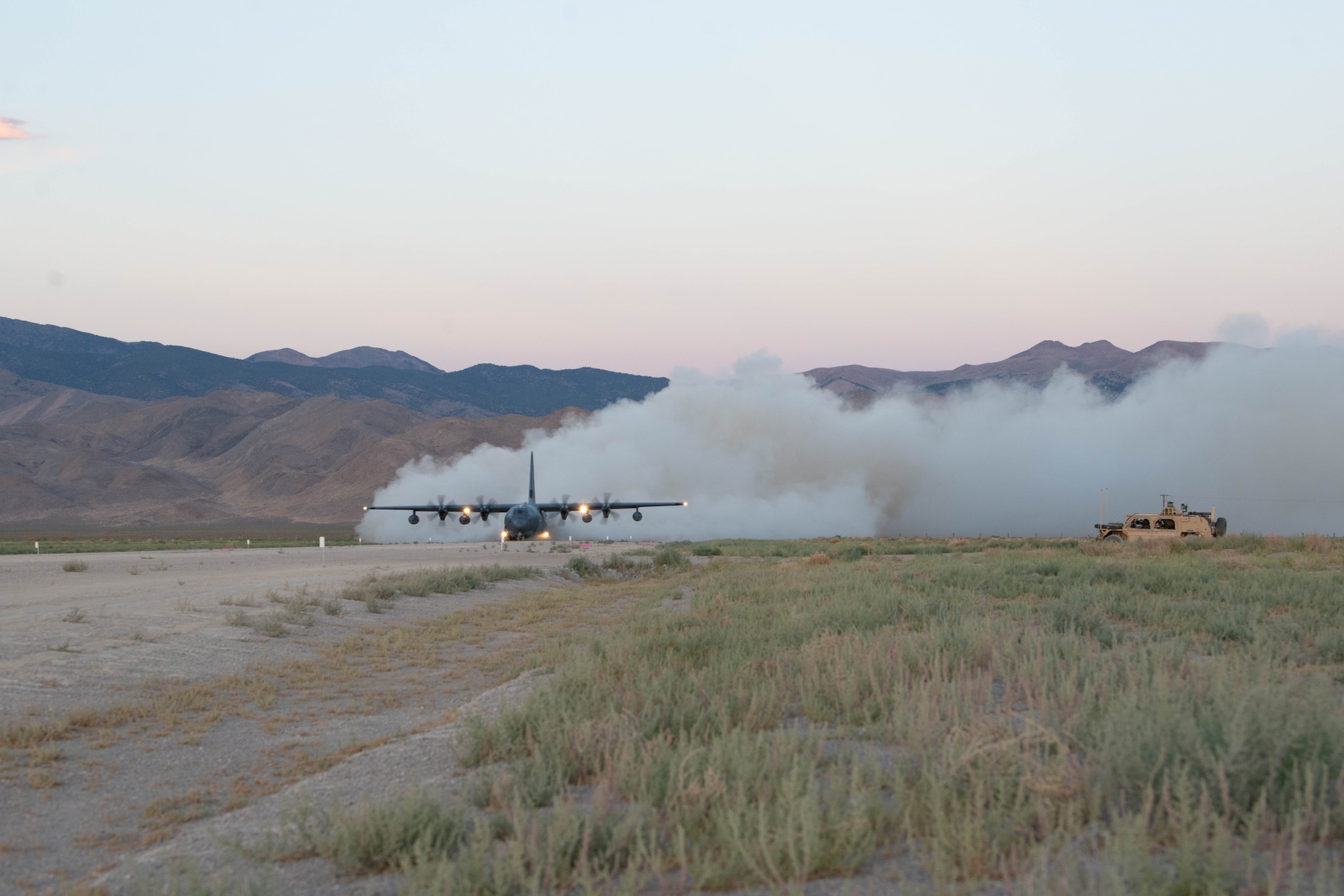 A military cargo aircraft lands on a dusty dirt landing strip.