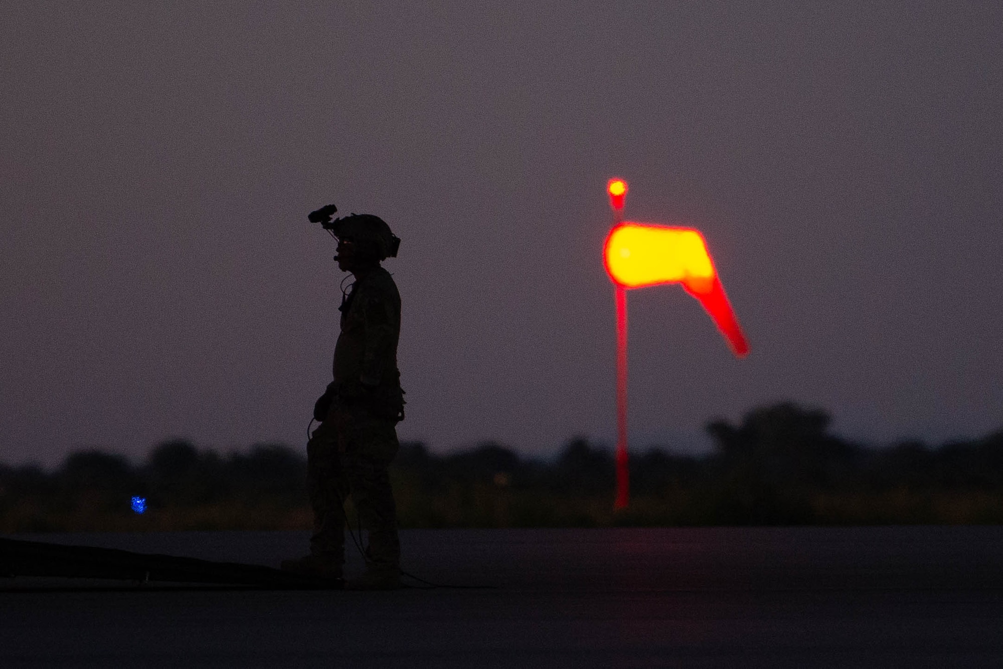 A man in military uniform and equipment stands in the setting sun.