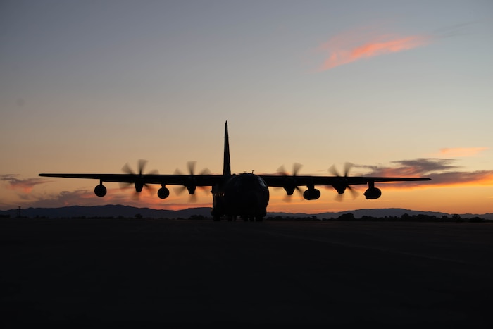 A military cargo aircraft taxis on a dirt landing strip.