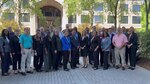 Group of professional dressed people standing on a lightly colored brick pathway outside in front of a building.
