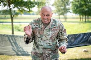 A man in a U.S. Air Force uniform grits his teeth, making a face. In between his teeth, parts of an insect.