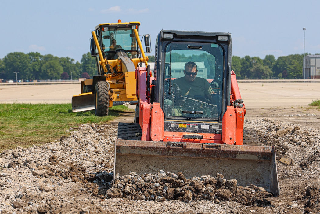 Two Airmen in backhoes pushing dirt on the runway.