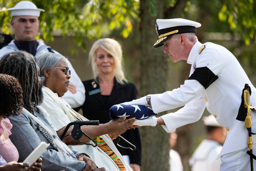 A civilian is handed the American flag by a Navy officer.