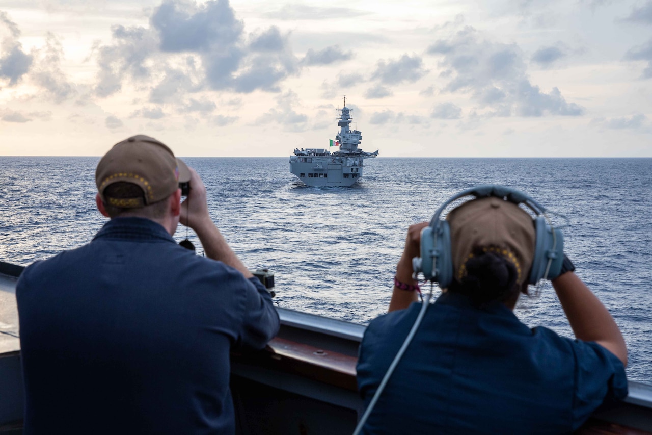 Sailors look through binoculars while aboard a ship at sea.