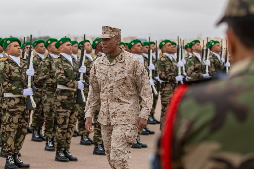 A Marine walks in front of a foreign military honor guard.