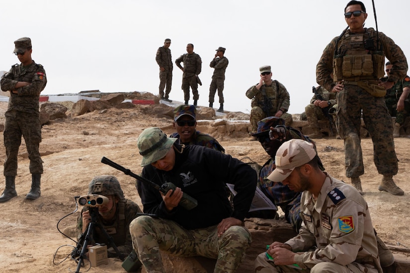 Soldiers speak into a radio while sitting atop a Moroccan hilltop.