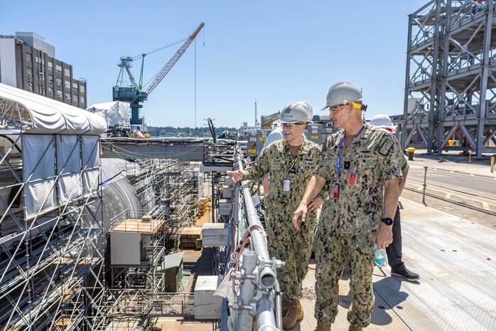 Rear Adm. Todd Weeks, program executive officer, Strategic Submarines, and Capt. Tim Clark, program manager, In Service Strategic Submarines, Naval Sea Systems Command, observe maintenance operations in Dry Dock 4 July 16, 2024, during a visit with the various submarine project teams at Puget Sound Naval Shipyard & Intermediate Maintenance Facility in Bremerton, Washington. (U.S Navy photo by Jeb Fach)