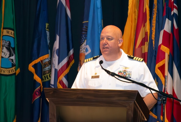 Navy captain in dress whites speaks during change of command ceremony.