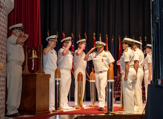 Navy captain salutes during departure as six sideboys in Navy whites return salute.