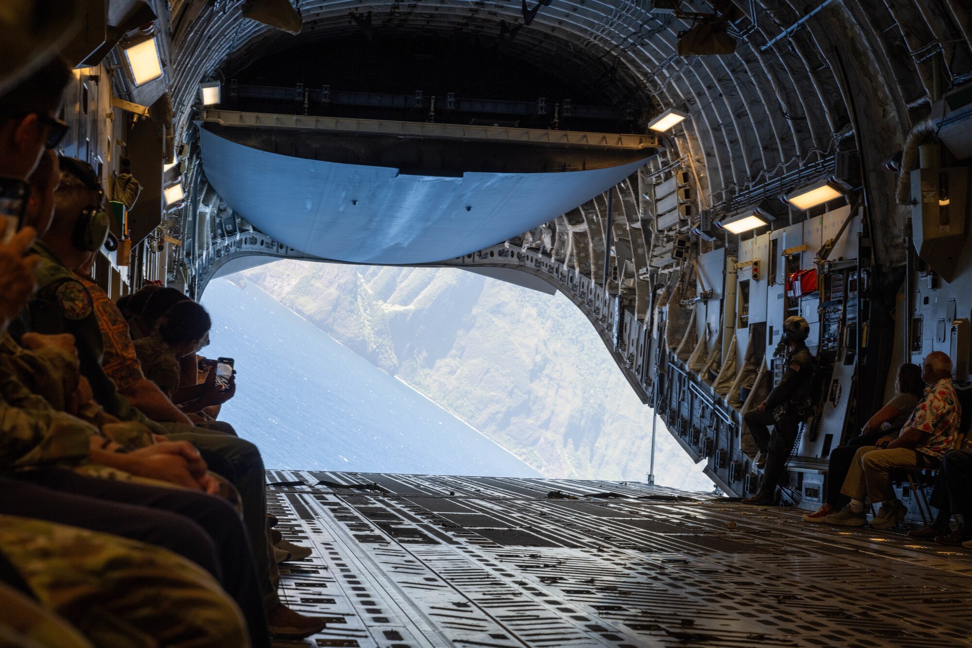 Airmen and civilians sit in a military aircraft.