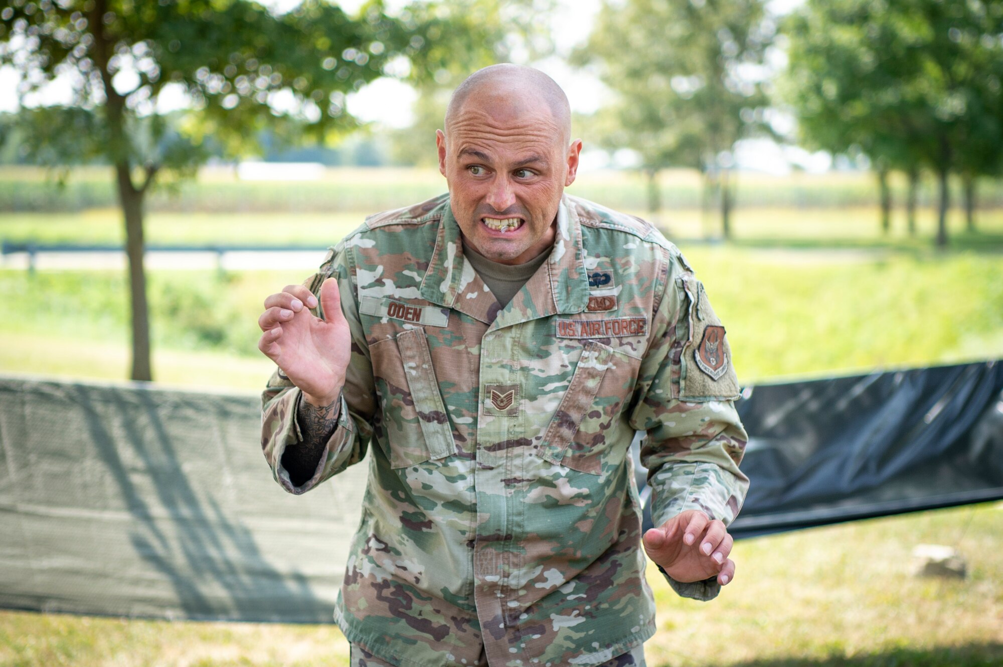 A man in a U.S. Air Force uniform grits his teeth, making a face. In between his teeth, parts of an insect.