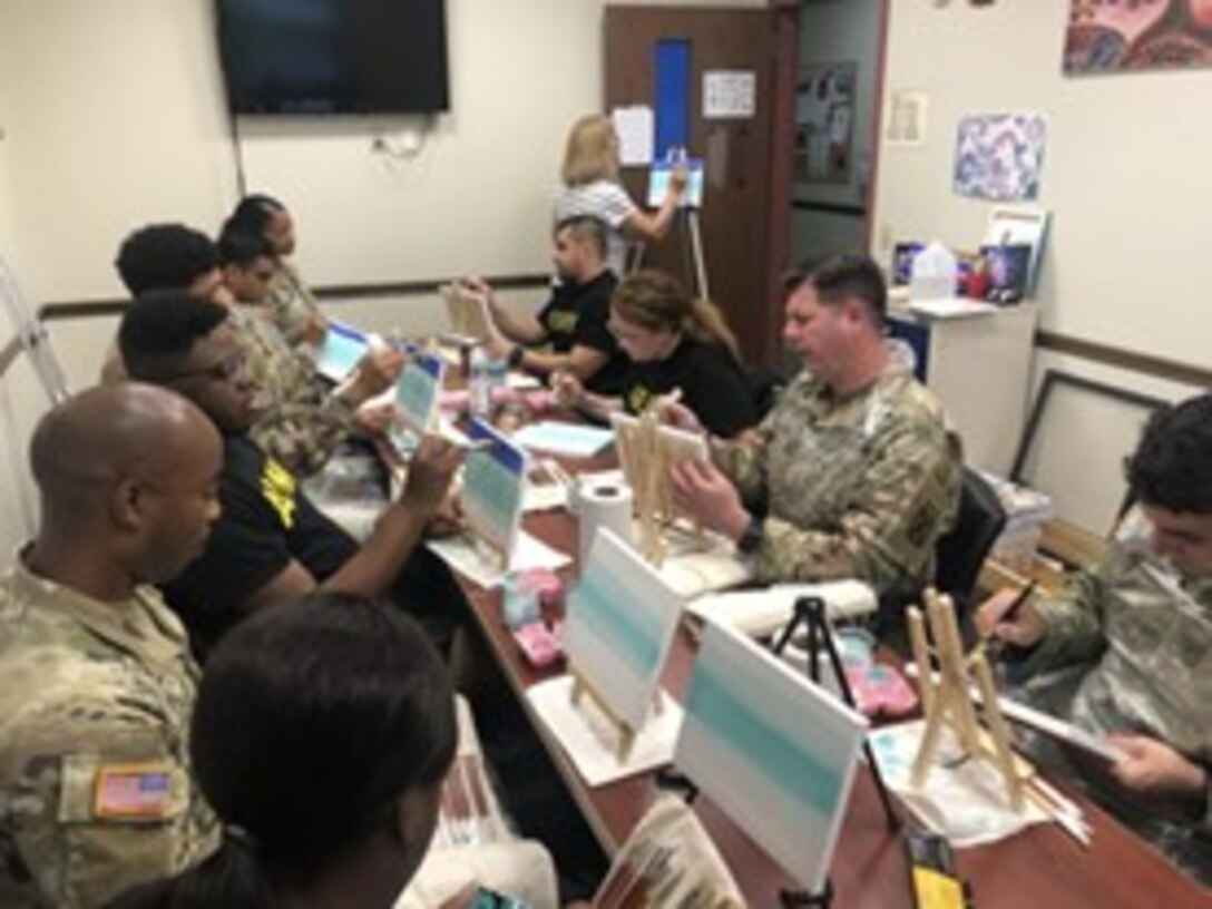 Spc Dominique Washington, just under the TV screen, watches art instruction from Teresa Kramer