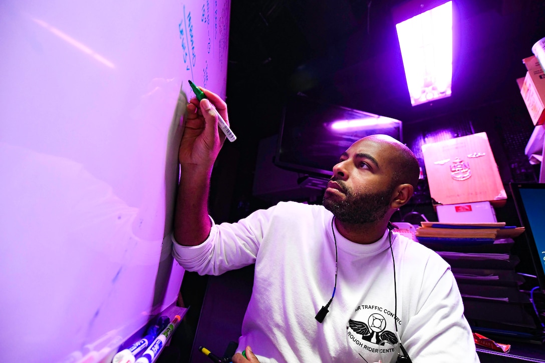 A sailor uses a marker to write on a whiteboard inside a Navy ship.