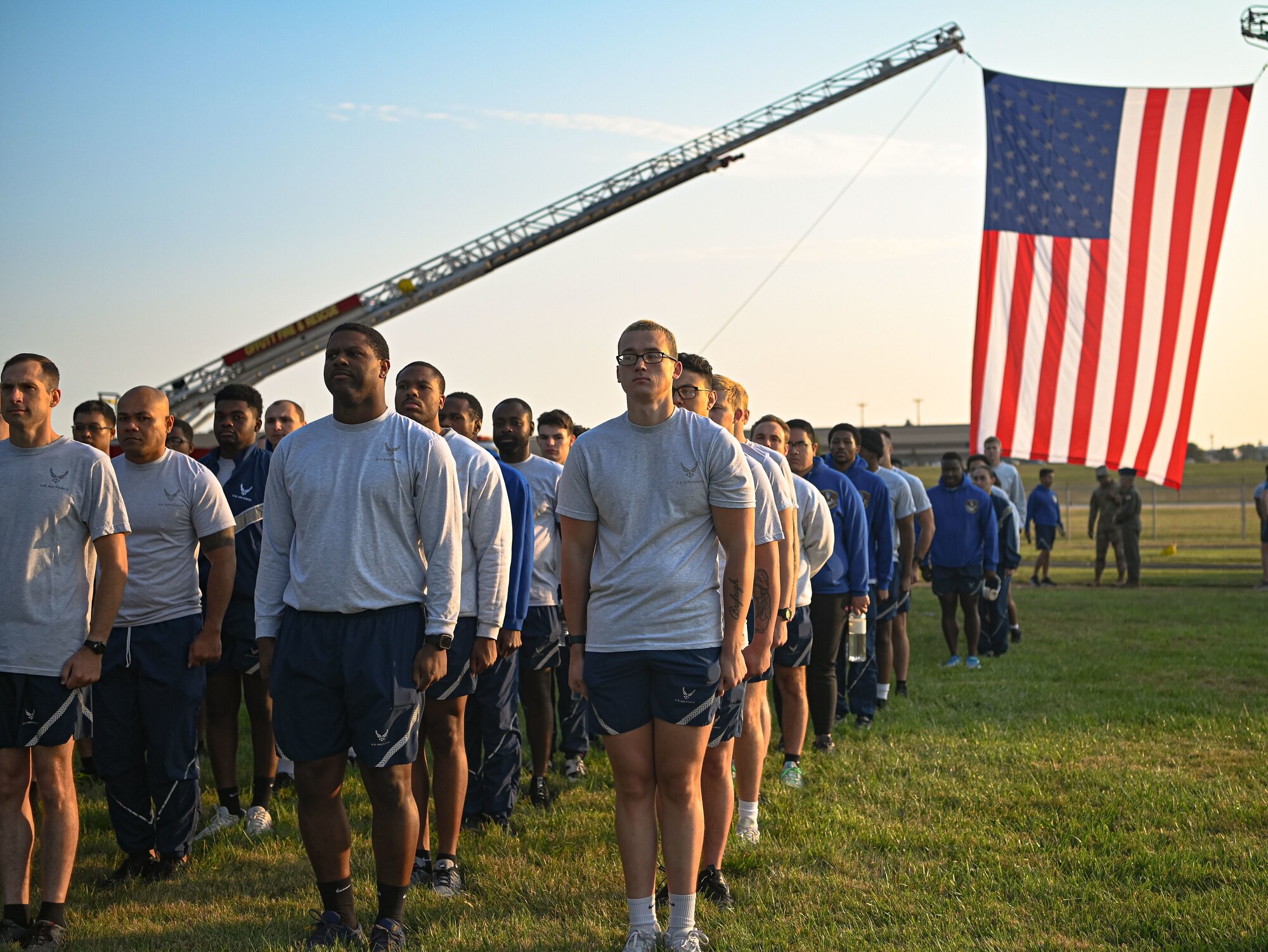 People stand in formation in front of an American flag