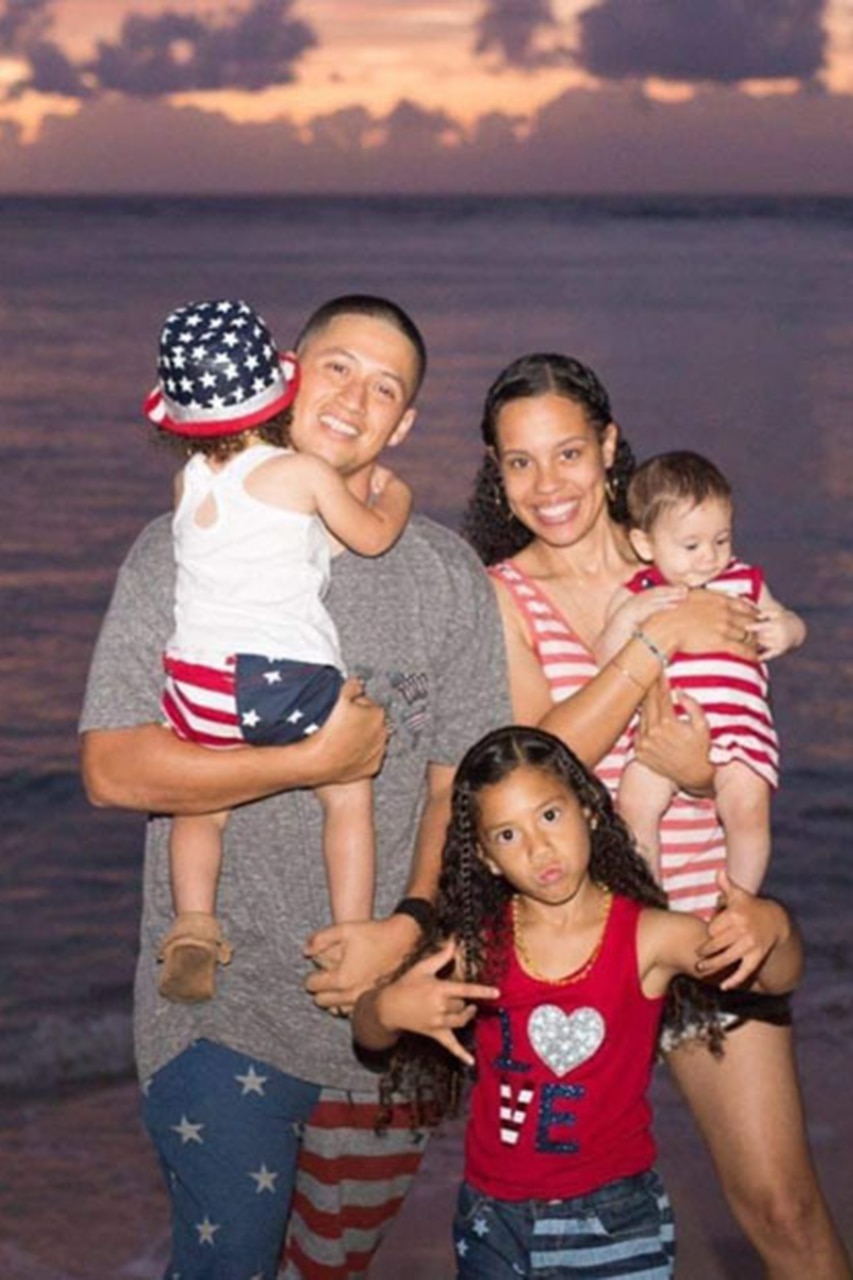 A couple and three children smile for the camera with the ocean in the background at twilight.