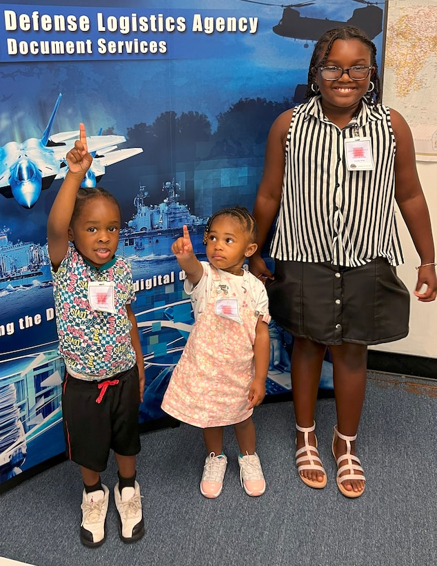 Three children standing in front of a DLA Doc Services banner