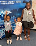Three children standing in front of a DLA Doc Services banner