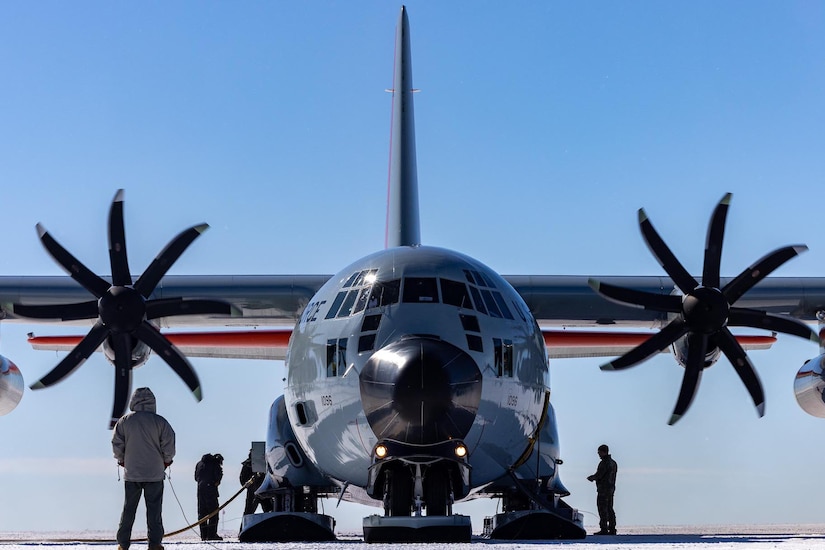 An LC-130 Hercules aircraft sits on the ground as service members stand around it.