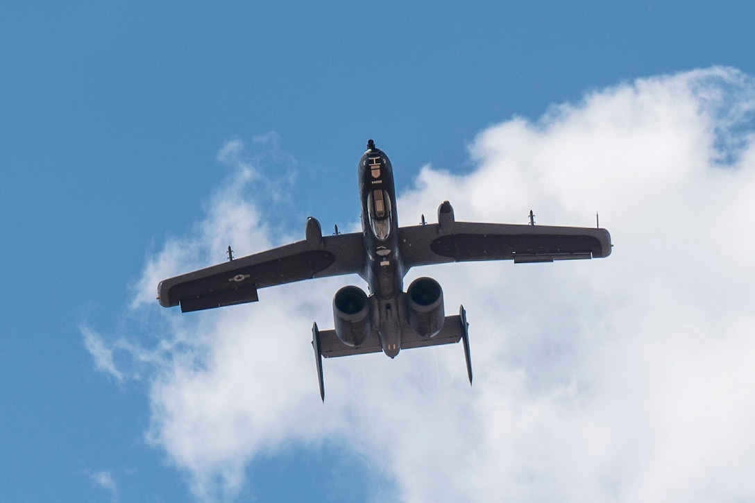 An aircraft performs a maneuver in a cloudy sky as seen from below.