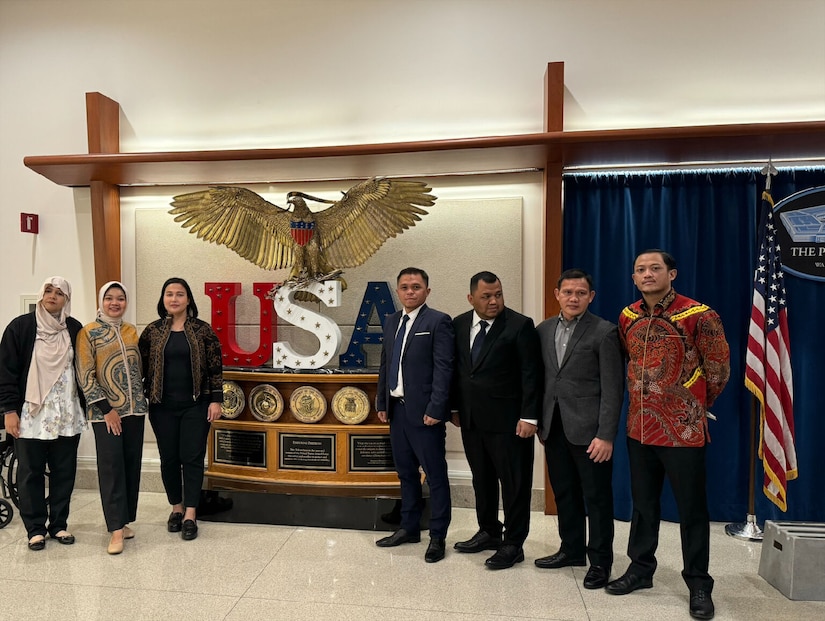 A group of men and women wearing civilian attire stand next to a statue of an eagle.