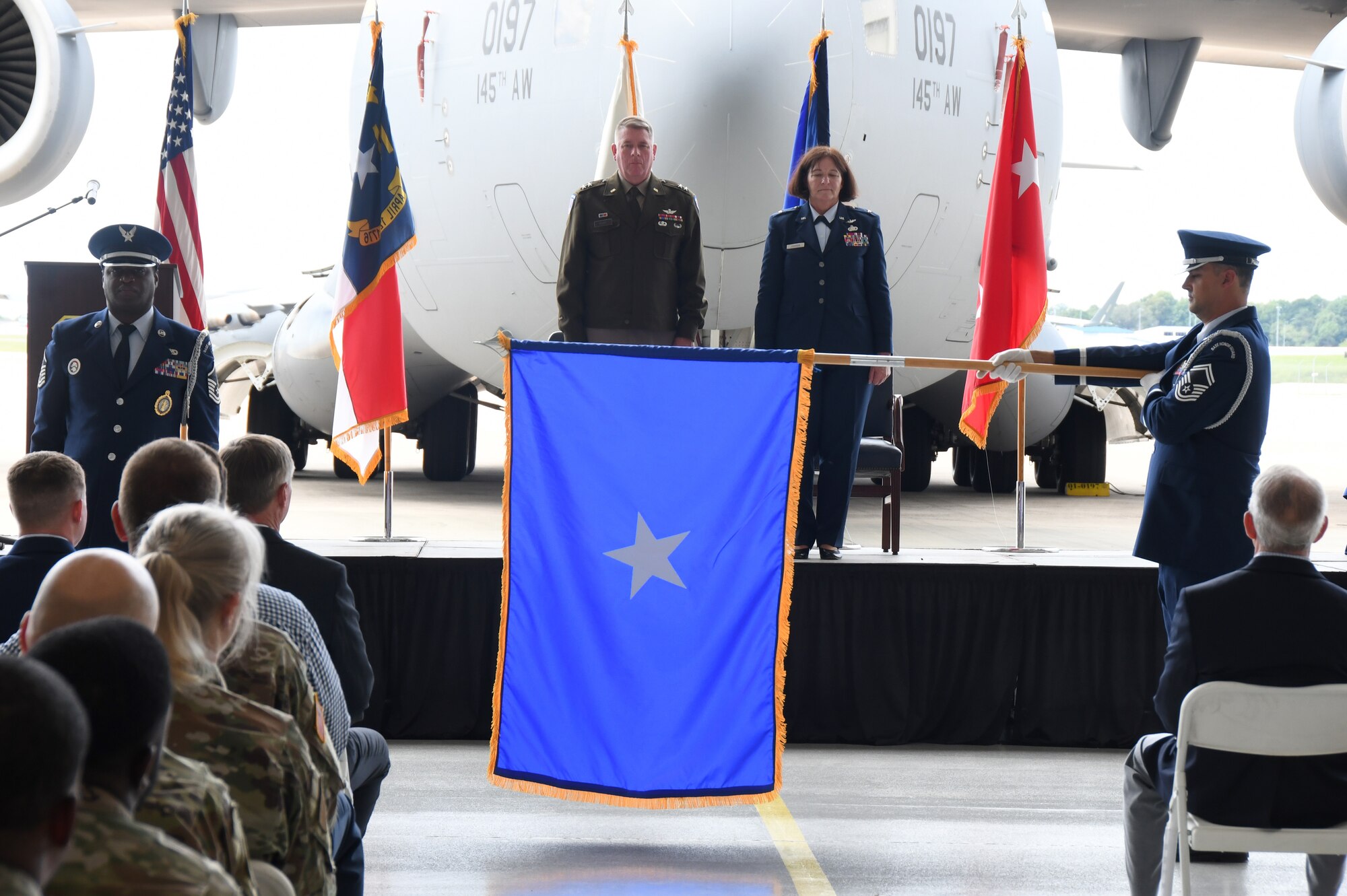 U.S. Army Maj. Gen. Todd Hunt, the Adjutant General of the North Carolina National Guard, left, and U.S. Air Force Brig. Gen. Shawne M. Johnson, Chief of Staff for the North Carolina Air National Guard (NCANG) watch as an Air Force one-star flag is unfurled during her promotion ceremony held inside a C-17 Globemaster III hangar held at the Charlotte-Douglas International Airport base, Sept. 8, 2024.