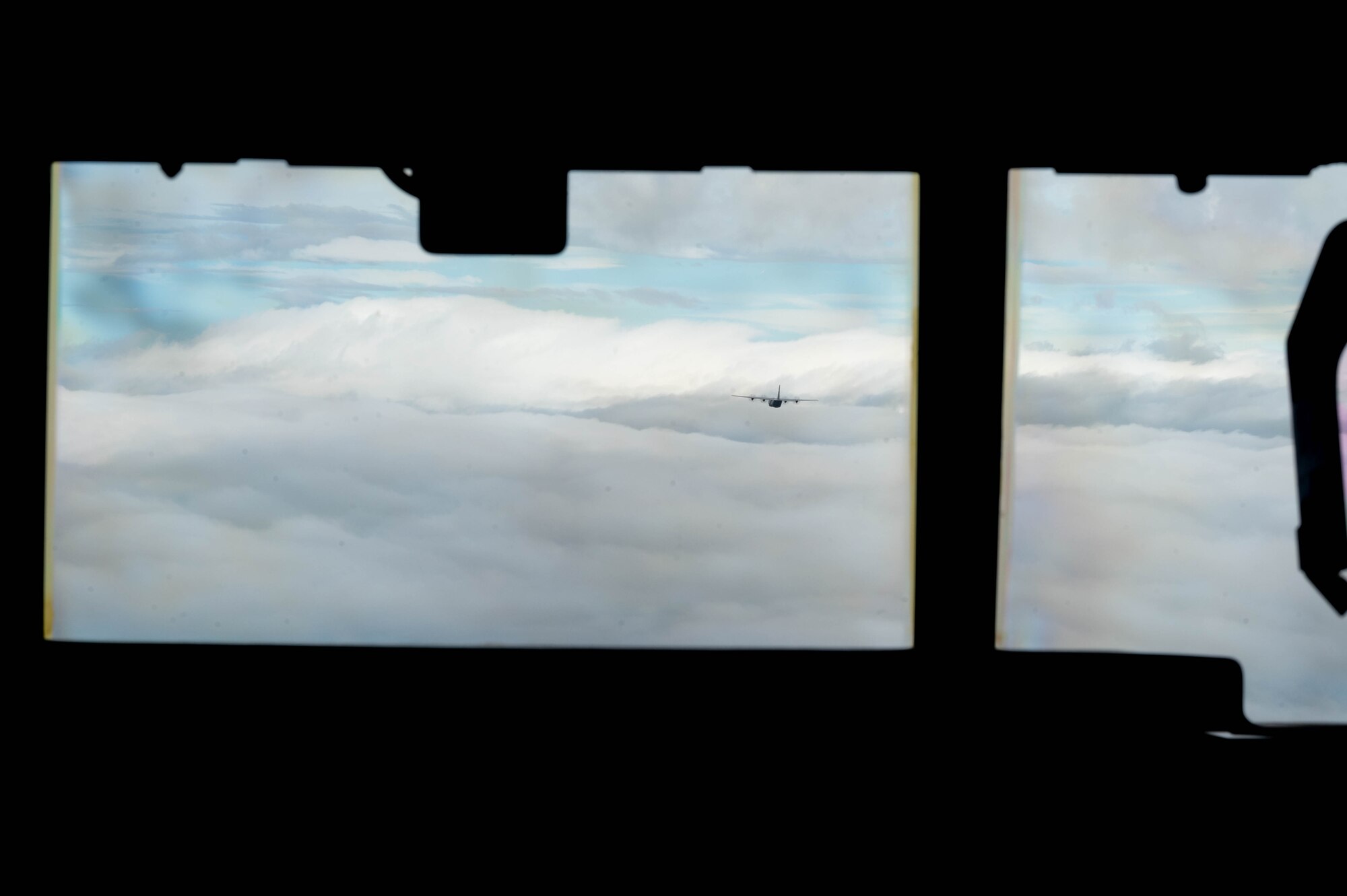 A pilot looks out the window of the cockpit at an aircraft flying in the distance.