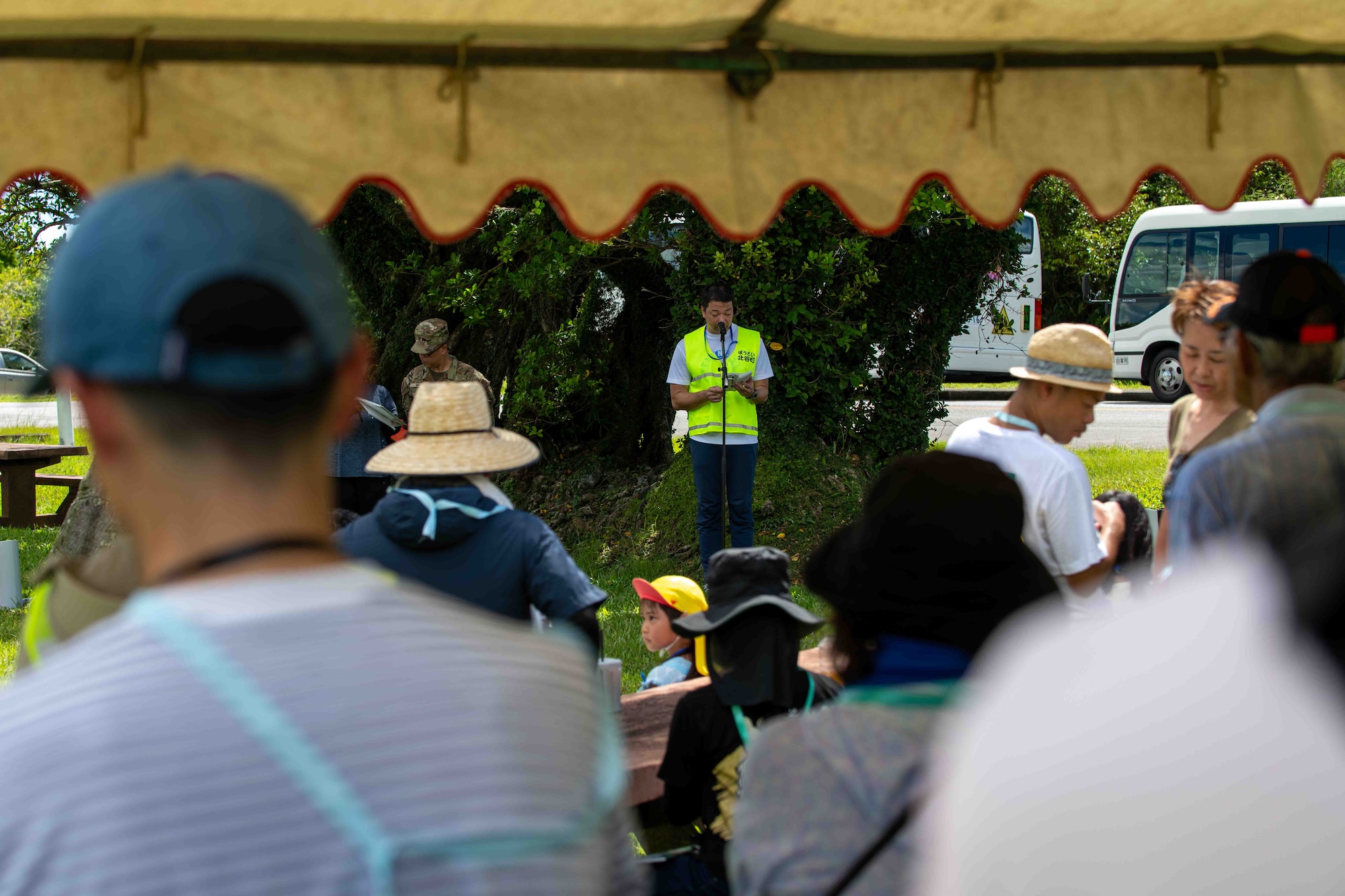 Person in a vest gives a speech in front of a crowd.