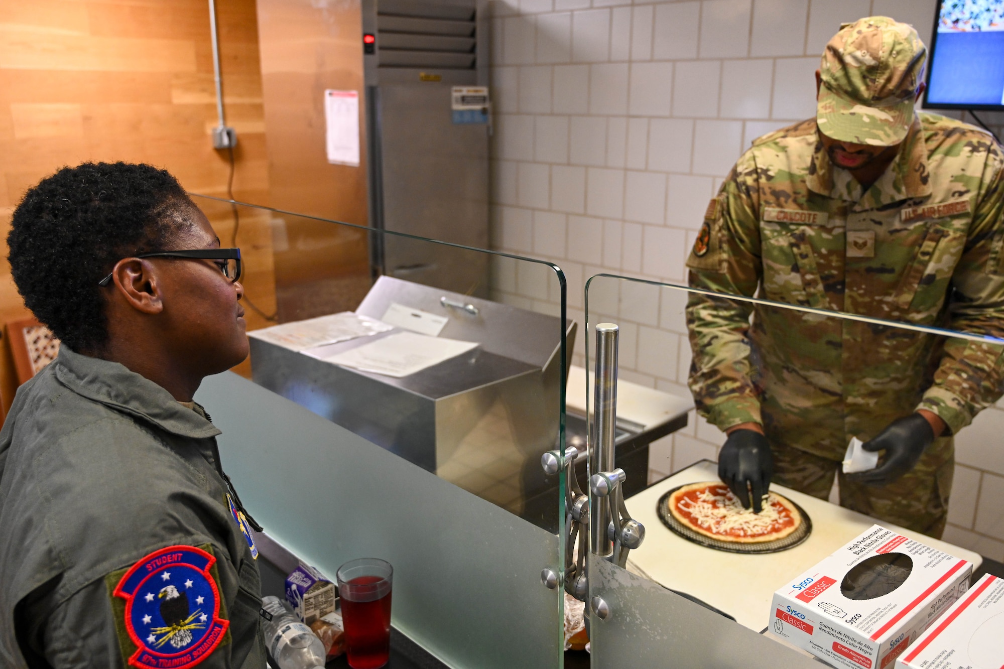 U.S. Air Force Staff Sgt. Victor Calcote, 97th Force Support Squadron dining facility manager, prepares a pizza for Airman 1st Class Dai’ja Sanders, 97th Training Squadron loadmaster student, at the Hangar 97 dining facility at Altus Air Force Base, Oklahoma, Sept. 6, 2024. The pizzas are made fresh to order and customizable with various toppings. (U.S. Air Force photo by Senior Airman Miyah Gray)