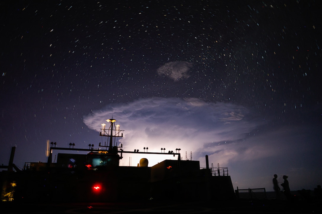 A ship sails at night under a partially cloudy sky with visible stars.