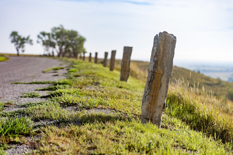 Grey rock formations stand in grass with grey gravel to the left, grass to the right and blue sky in the background.
