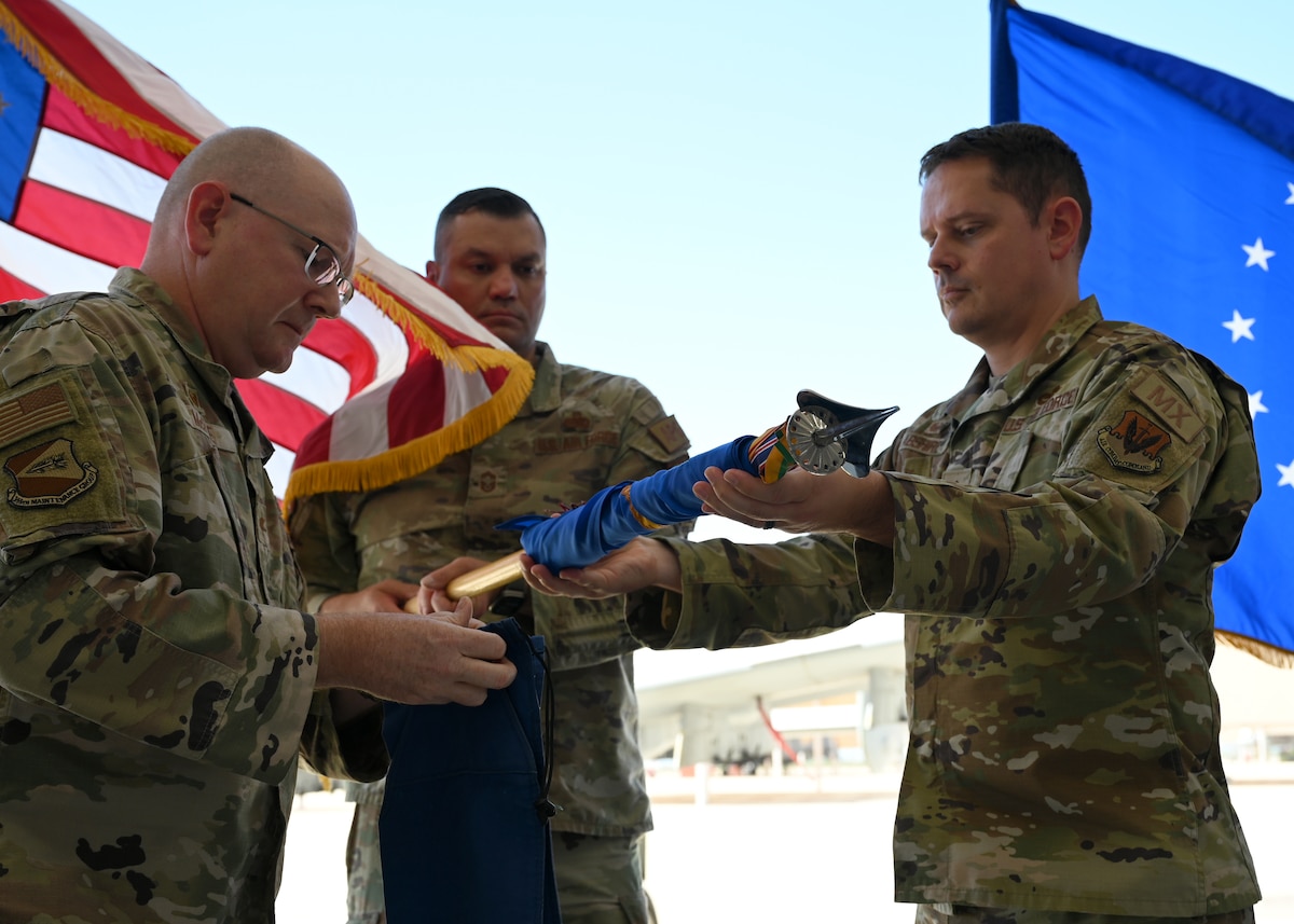 U.S. Air Force Maj. Benjamin Abshire, 354th Fighter Generation Squadron commander, right, sheaths the guidon with Col. Clarence McRae, 355th Maintenance Group commander, left, during the 354th FGS inactivation ceremony at Davis-Monthan Air Force Base, Arizona, Sept. 13, 2024. Sheathing the guidon is an Air Force tradition, which signifies that the squadron’s history and lineage was preserved with that flag. (U.S. Air Force photo by Staff Sgt. Abbey Rieves)