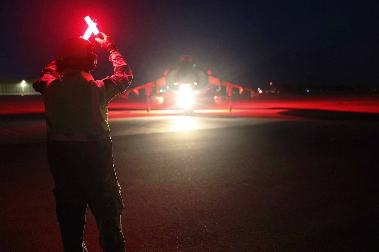 A Marine directs a jet on a runway at night.