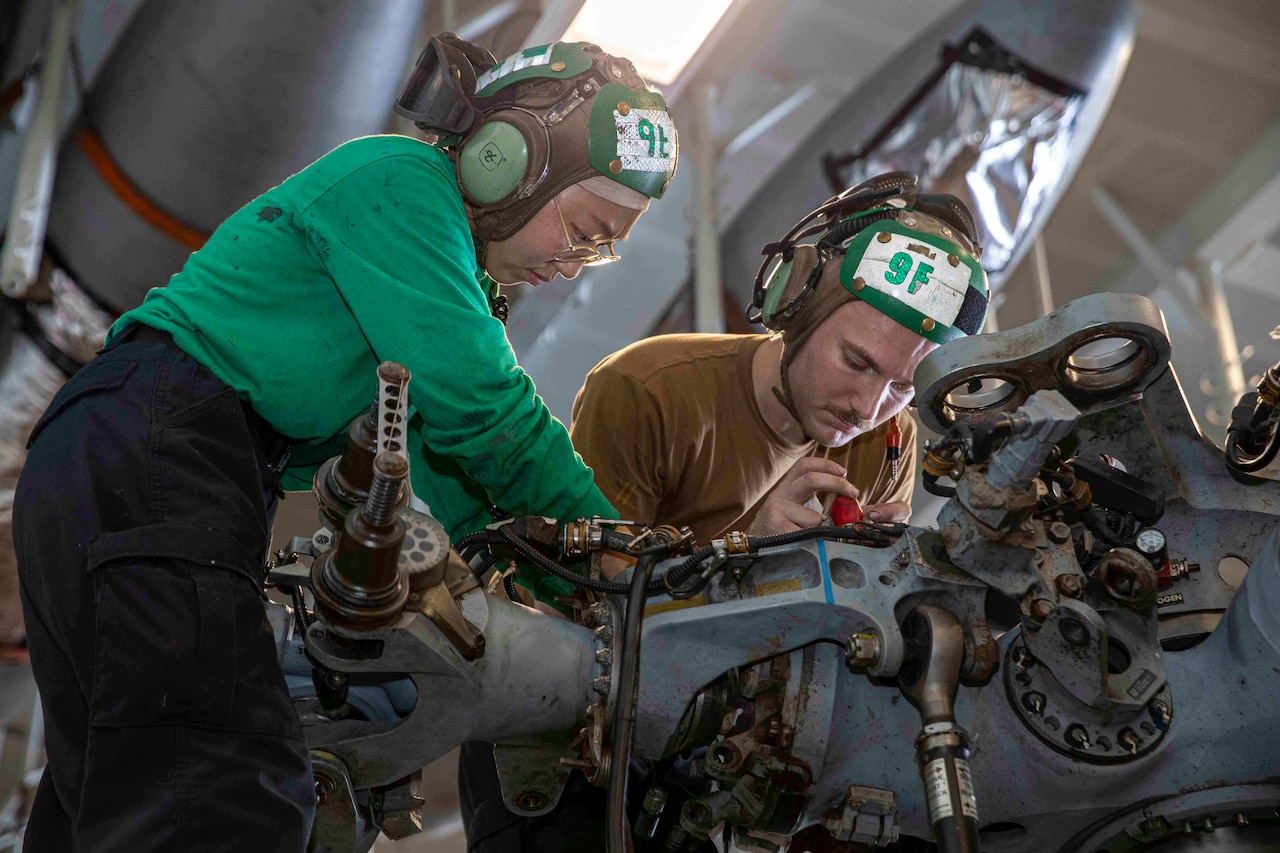 Sailors work on a piece of machinery inside a ship.
