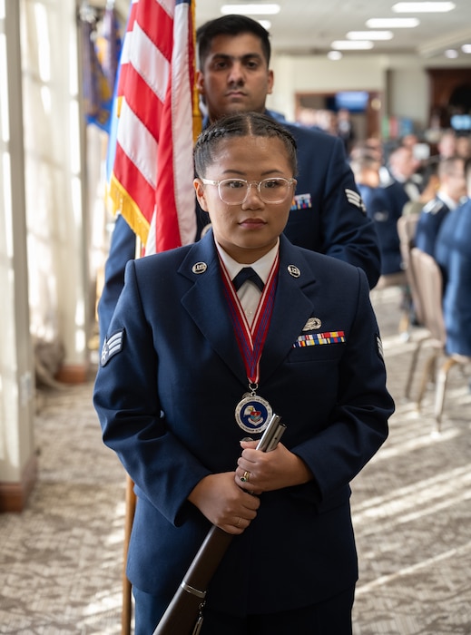 A woman in an Air Force service dress uniform and wearing a medallion, stands at the front of a line of Airmen.