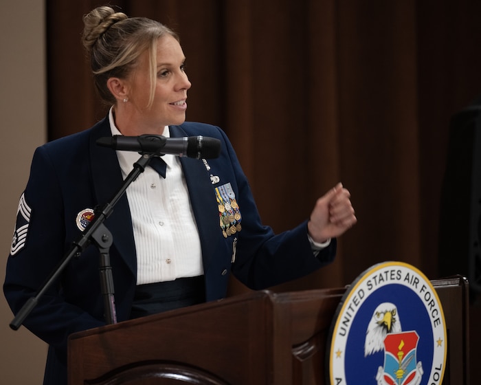 A woman in an Air Force Mess Dress Uniform speaks at a podium.