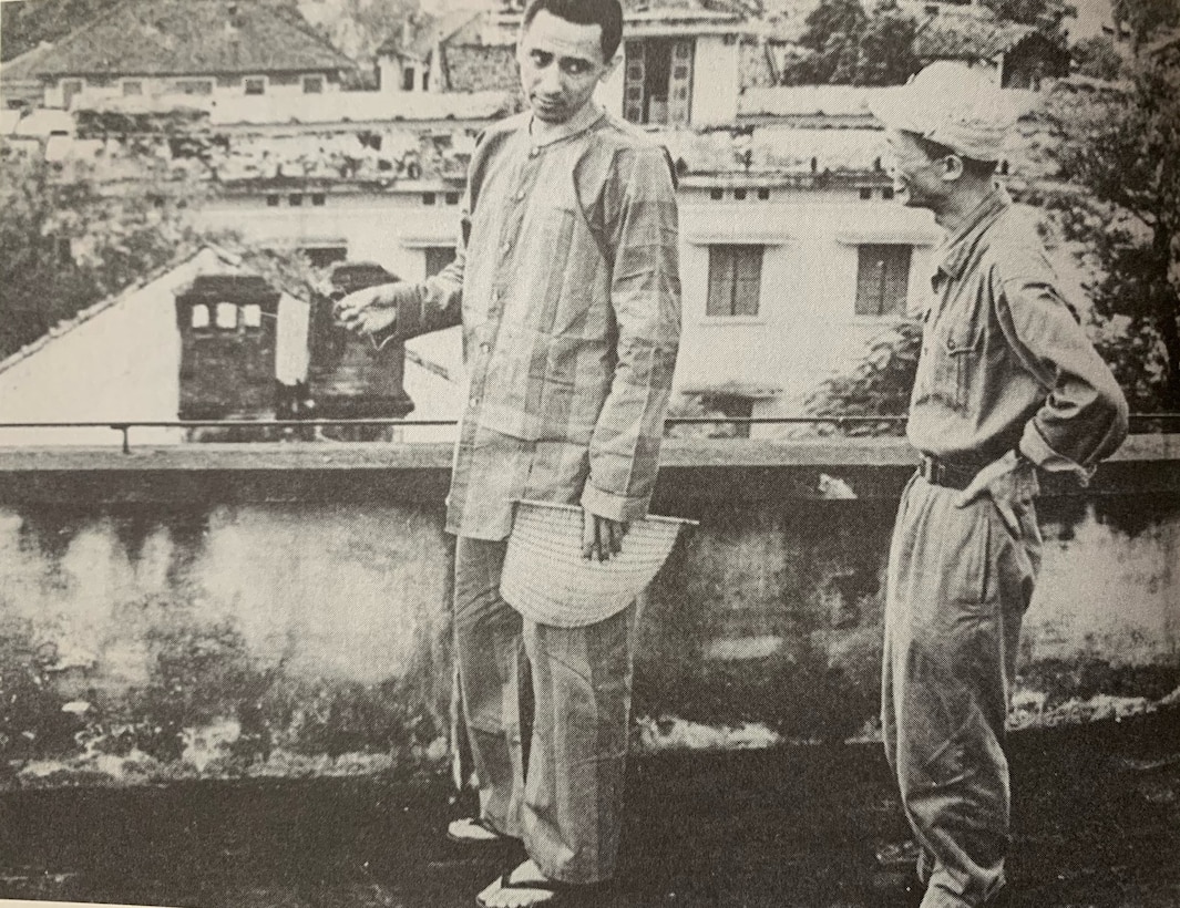 Lt. j.g. Everett Alvarez, Jr., in his striped prison uniform, talks with a Vietnamese prison guard while in downtown Hanoi, North Vietnam, ca. 1967. Vietnamese prison guards routinely escorted American POWs around town to view nationalist- and Communist-themed museum exhibits and other landmarks. They were often paraded before crowds of angry Vietnamese townspeople and photographed for propaganda purposes (Office of the Secretary of Defense).