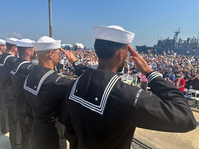 Sailors standing in formation salute a crowd.